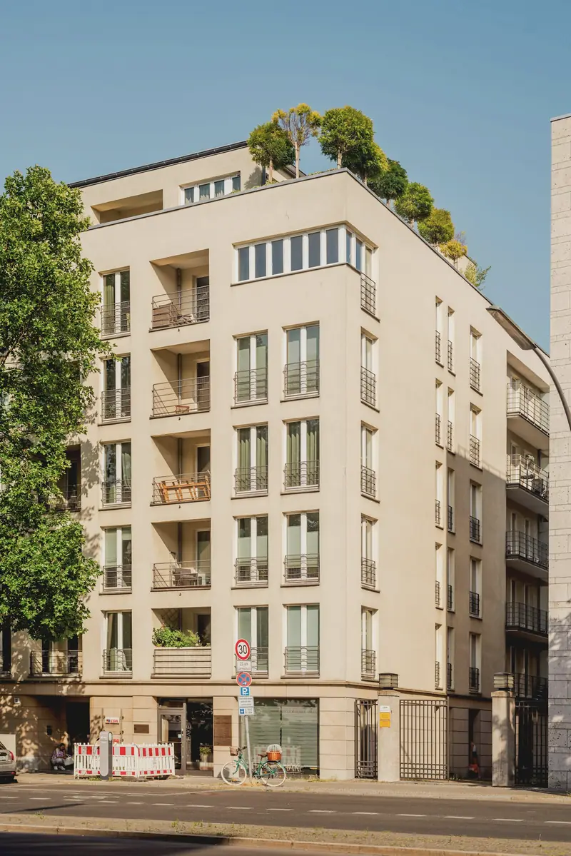 Modernes Mehrfamilienhaus mit begrünten Balkonen und Bäumen
