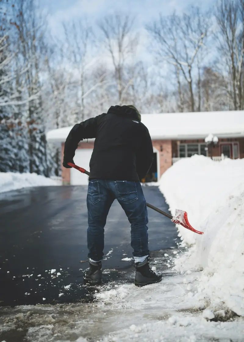 Person räumt mit einer Schneeschaufel eine verschneite Hauseinfahrt